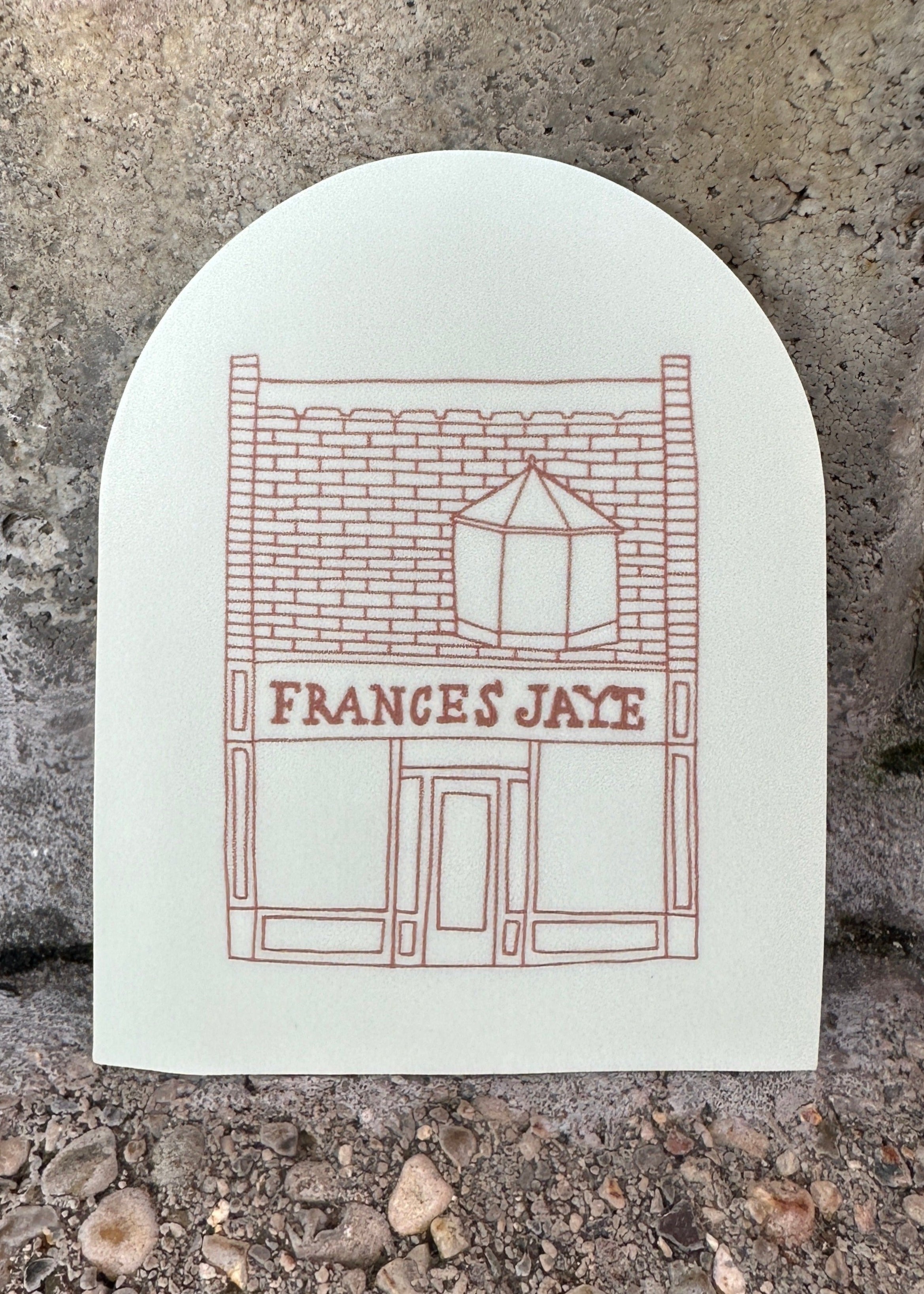 A cream colored arched sticker with Frances Jaye store front etched on it.