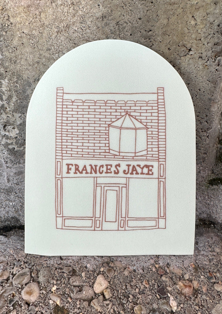 A cream colored arched sticker with Frances Jaye store front etched on it.