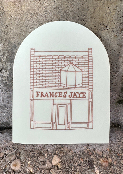 A cream colored arched sticker with Frances Jaye store front etched on it.